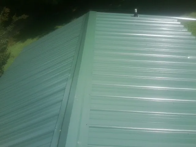 New green metal panels meeting at the ridge of a roof — Flat Roof Repair work by our crew in Maytown