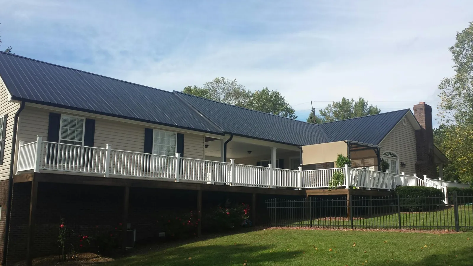Black metal roof above a long white railed deck on a hillside home in Maytown