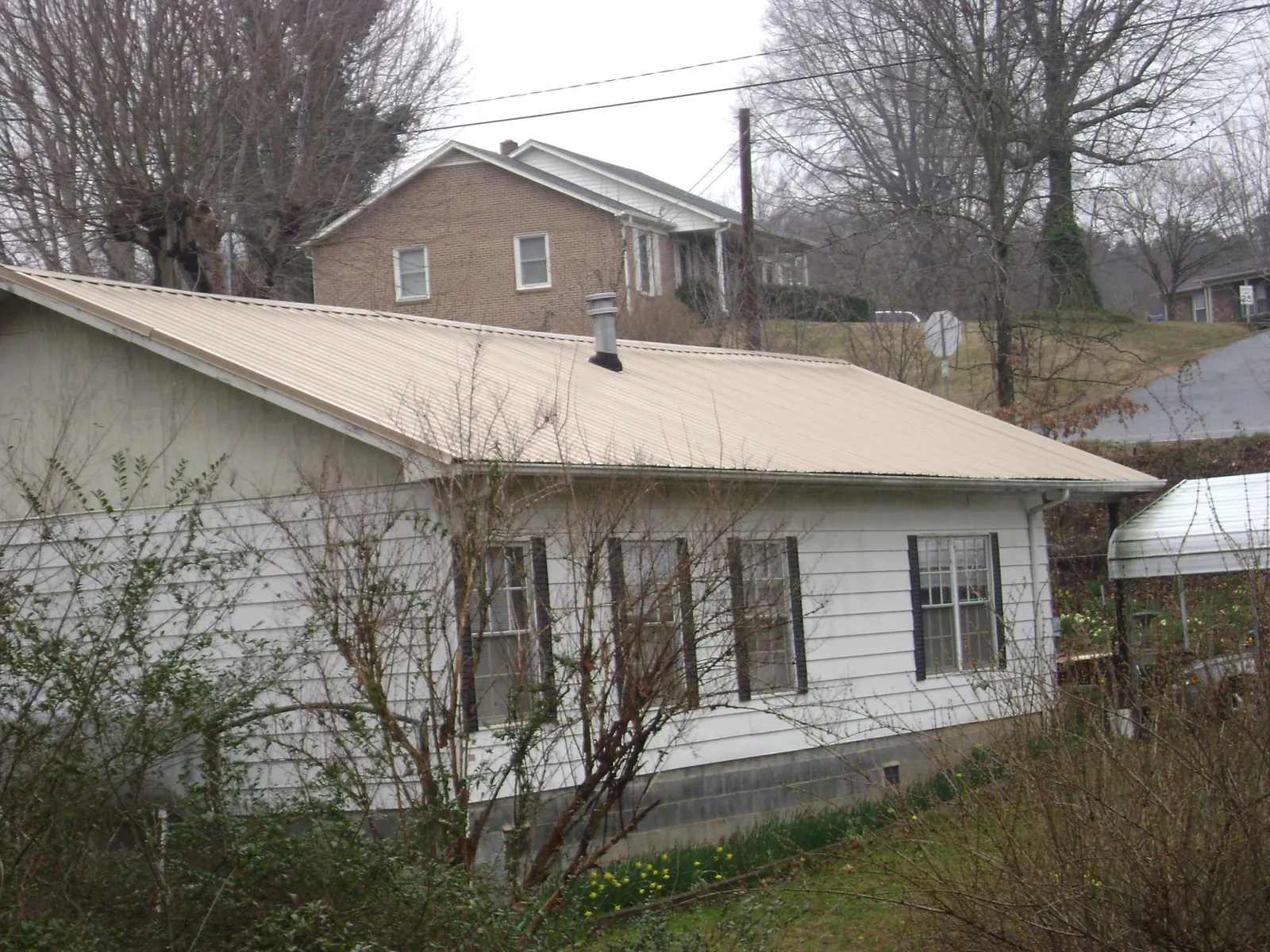 Tan metal roof on a white sided house set into a hillside — Commercial Roofing by Roofing Brothers in Maytown